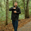 Man wearing a black waterproof Belgian army rain jacket with hood in a forest setting walking on a trail