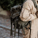 A person wearing an olive green Austrian military tactical backpack with multiple straps and compartments.