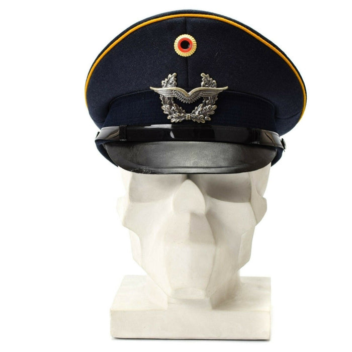 Vintageblå tyska Luftwaffes luftvapen med spetsad visirmössa med militära insignier och gult rör som visas på vit byst