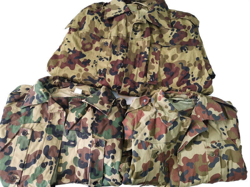 Three folded genuine Romanian Army M93 camouflage parkas in combat leaf pattern on white background