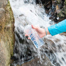 Hand holding Katadyn BeFree 0.6L water bottle filter under flowing stream water for instant filtration.