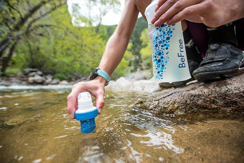 Person filling Katadyn BeFree 1.0L water filter bottle from a clear outdoor stream for clean drinking water.