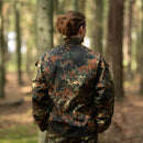 Back view of person wearing MFH Brand U.S. Military style flecktarn camo ripstop jacket in forest setting