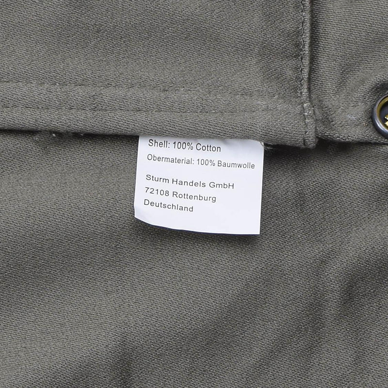 Close-up of MIL-TEC parka label showing 100% cotton shell material and German manufacturing details.