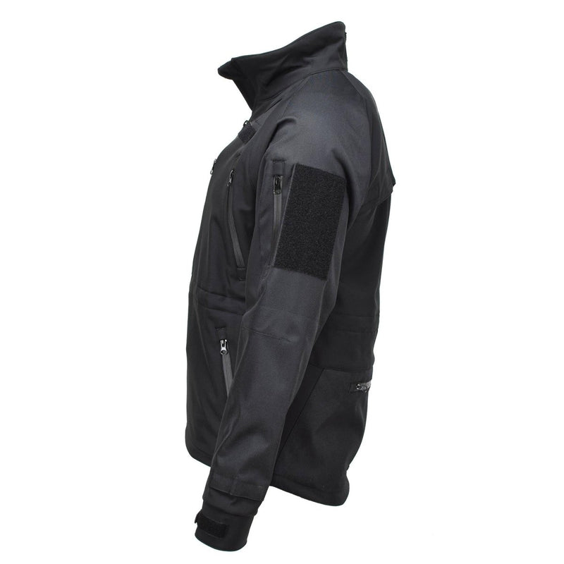 Black MIL-TEC softshell jacket with zippered pockets, vented armpits, and water-resistant fabric for tactical and outdoor use.