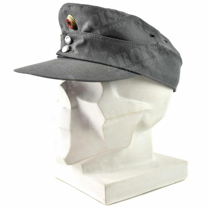 Original tysk armé bergsmössa i grått med spetsad front och metallbeteckningar på ett vitt skyltdockahuvud