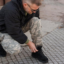 Man wearing original U.S. military digital camouflage field pants tying black tactical boots outdoors on pavement.