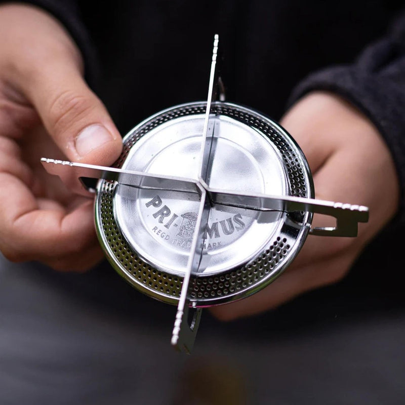 Close-up of a person holding the compact Primus ClassicTrail Stove 130 camping burner with four pod wide flame design.