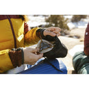 Person removing the compact Primus Essential Trail Stove from a black storage pouch outdoors in a snowy setting